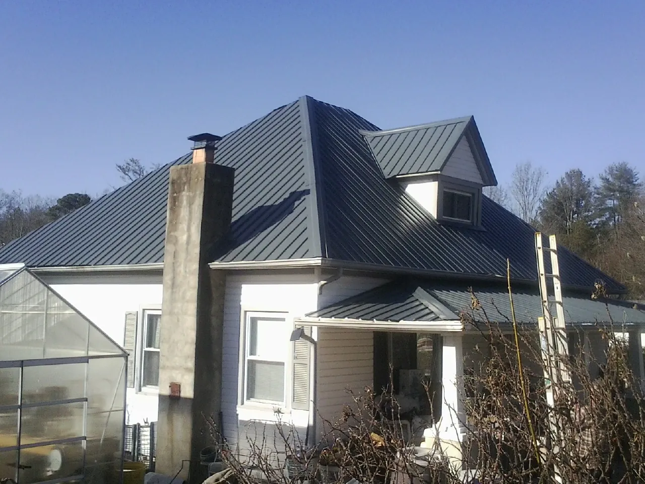 Dark blue standing seam metal roof on a white farmhouse with dormer — Slate & Tile Roof Repair by Roofing Brothers in Snow Hill