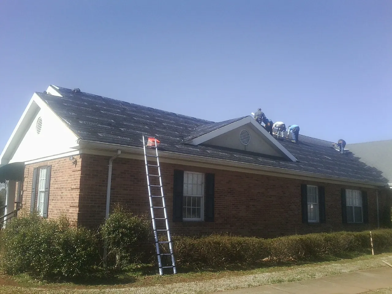 Crew tearing shingles off a brick ranch roof with a ladder set — Emergency Roof Repair work by our crew in Snow Hill
