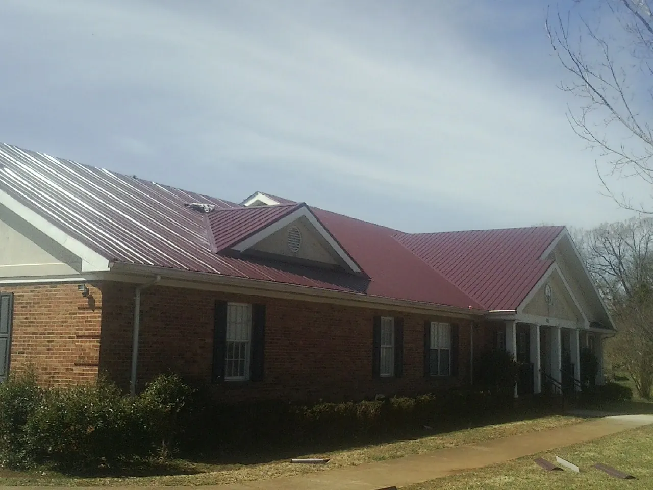 Red metal roof with gabled entries on a long brick building, from a Hail Damage Roof Repair job in Snow Hill