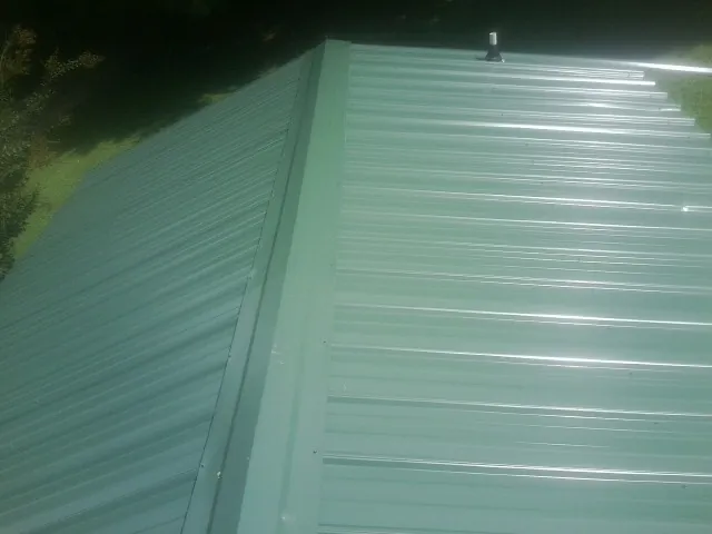 New green metal panels meeting at the ridge of a roof — Flat Roof Repair work by our crew in Snow Hill